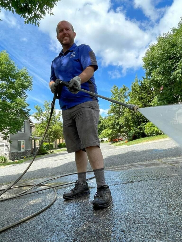 Man in a blue shirt pressure washing a driveway